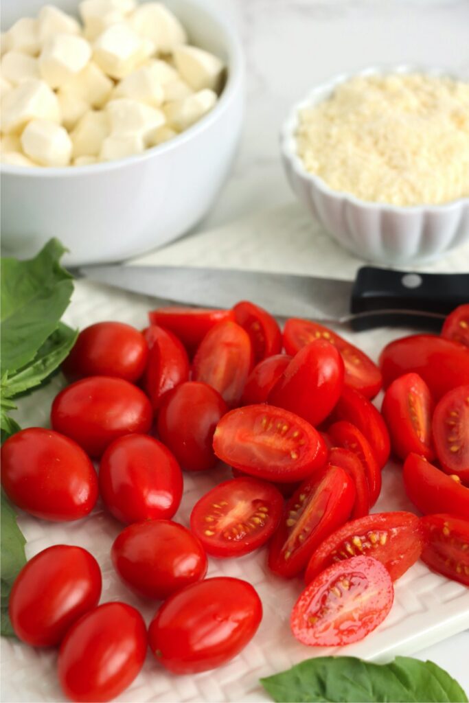 Closeup shot of cherry tomato halves in front of bowlful of parmesan cheese and bowlful of mozzarella pearls