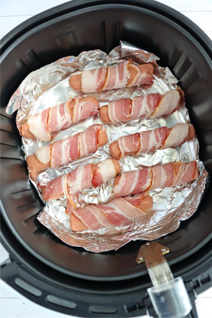 Overhead shot of uncooked bacon wrapped hot dogs in air fryer basket