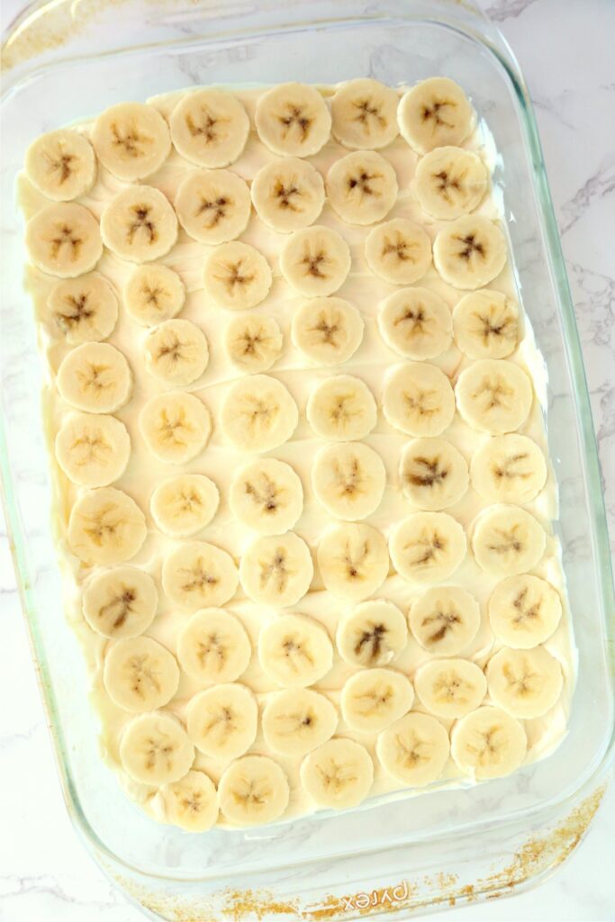 Overhead shot of layer of bananas over banana pudding cream cheese mixture in baking dish