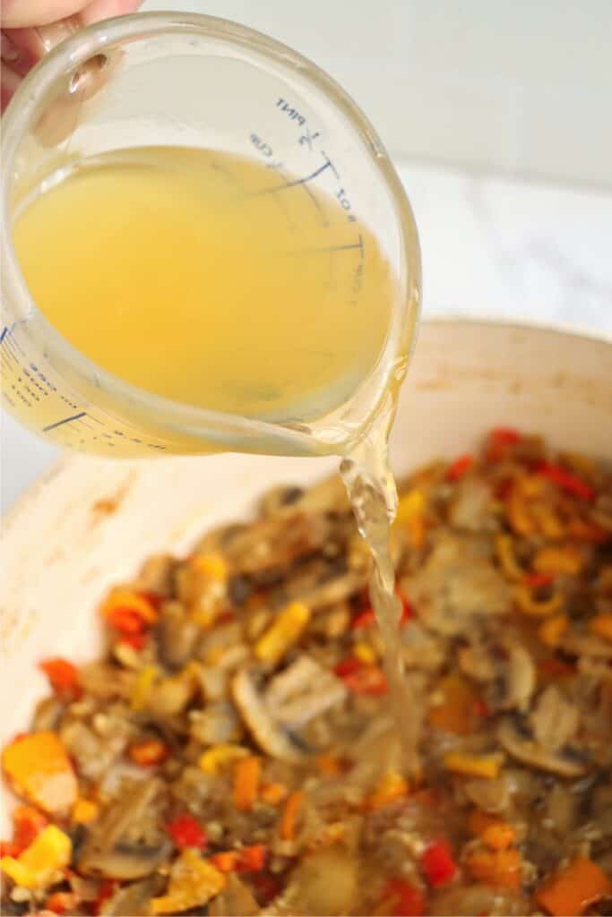 Broth being poured into panful of veggies. 