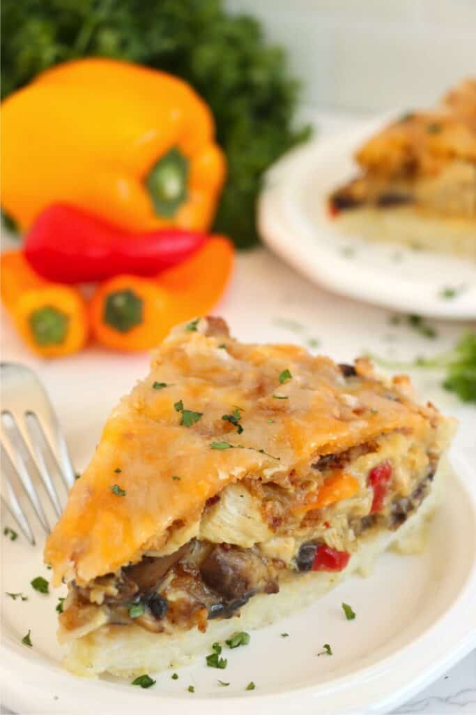 Slice of chicken rice crust pie on plate with peppers in background.