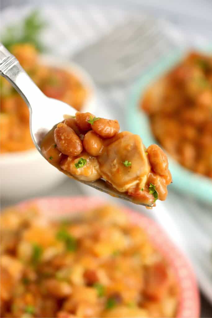 Closeup shot of spoonful of beans bacon and chicken skillet over bowl with more beans and chicken