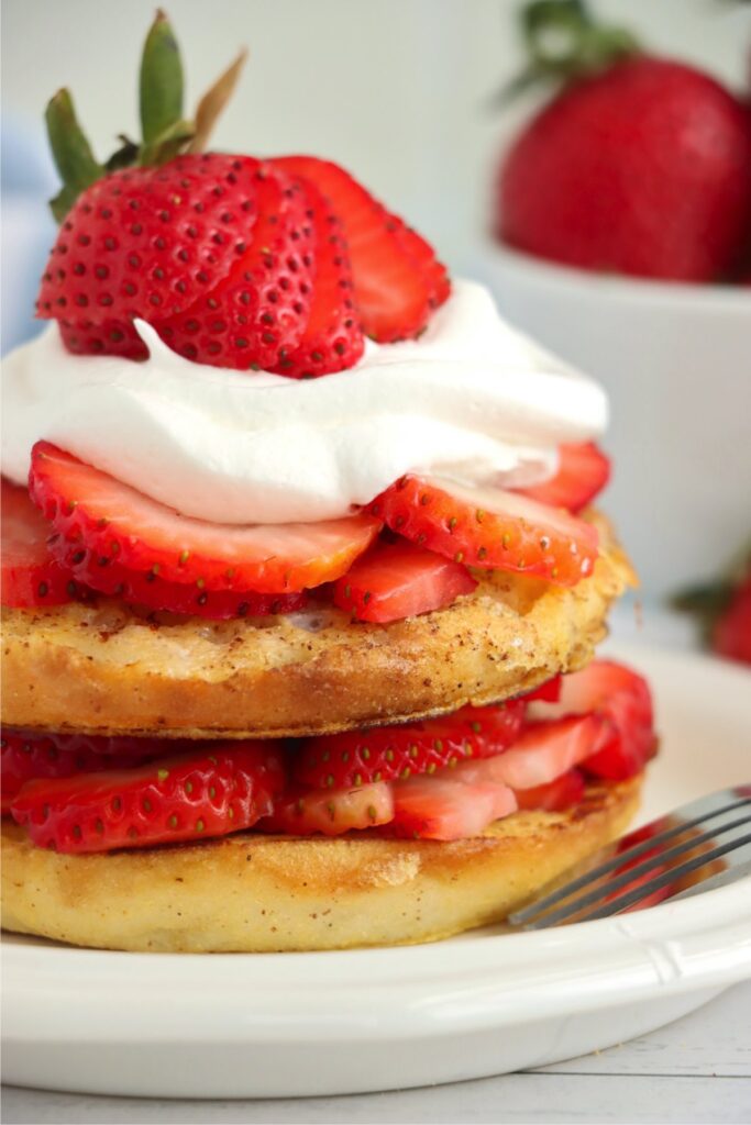 Closeup shot of English muffin French toast topped with strawberries and whipped cream on plate