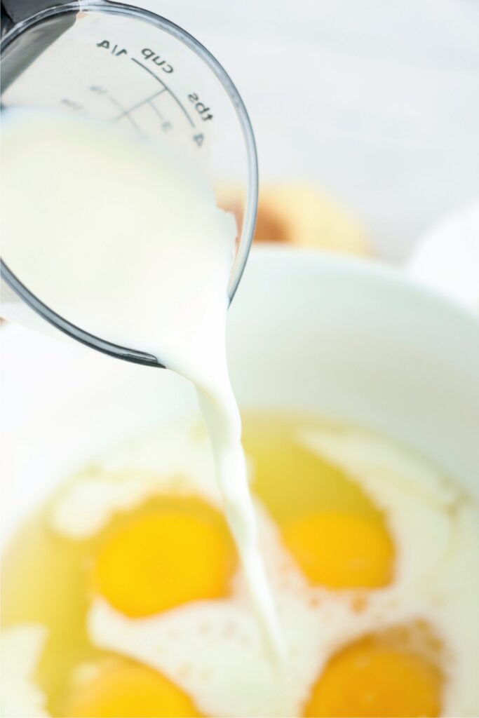 Closeup shot of milk being poured into bowlful of eggs.