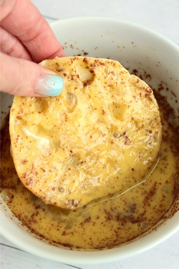 Closeup shot of English muffin half soaked in egg and cinnamon mixture. 