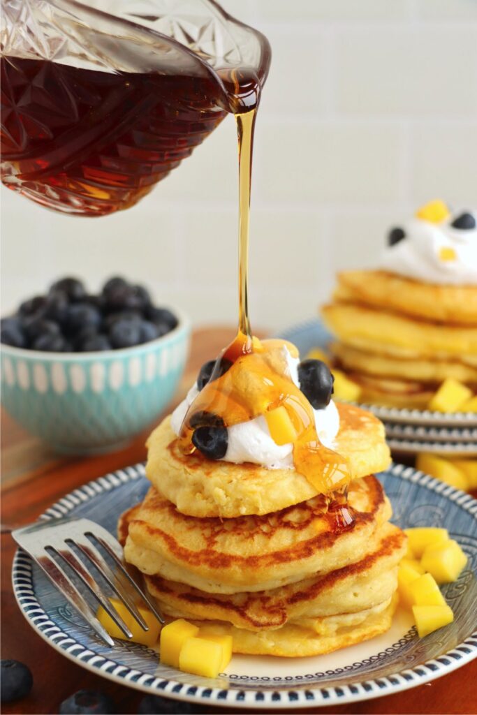 Stack of mango pancakes on plate being drizzled with syrup. 
