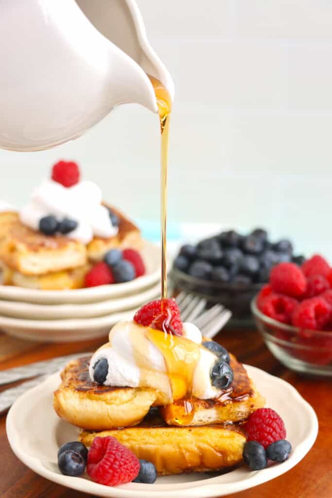 Stack of hot dog bun French toast on plate being drizzled with syrup