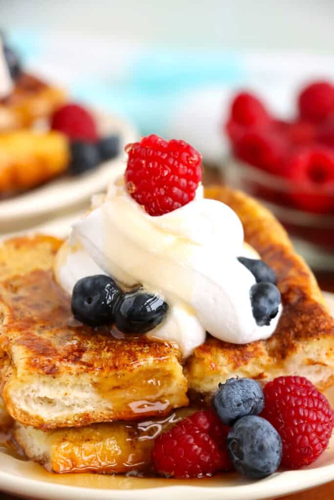 Closeup shot of hot dog French toast topped with whipped cream and berries on plate