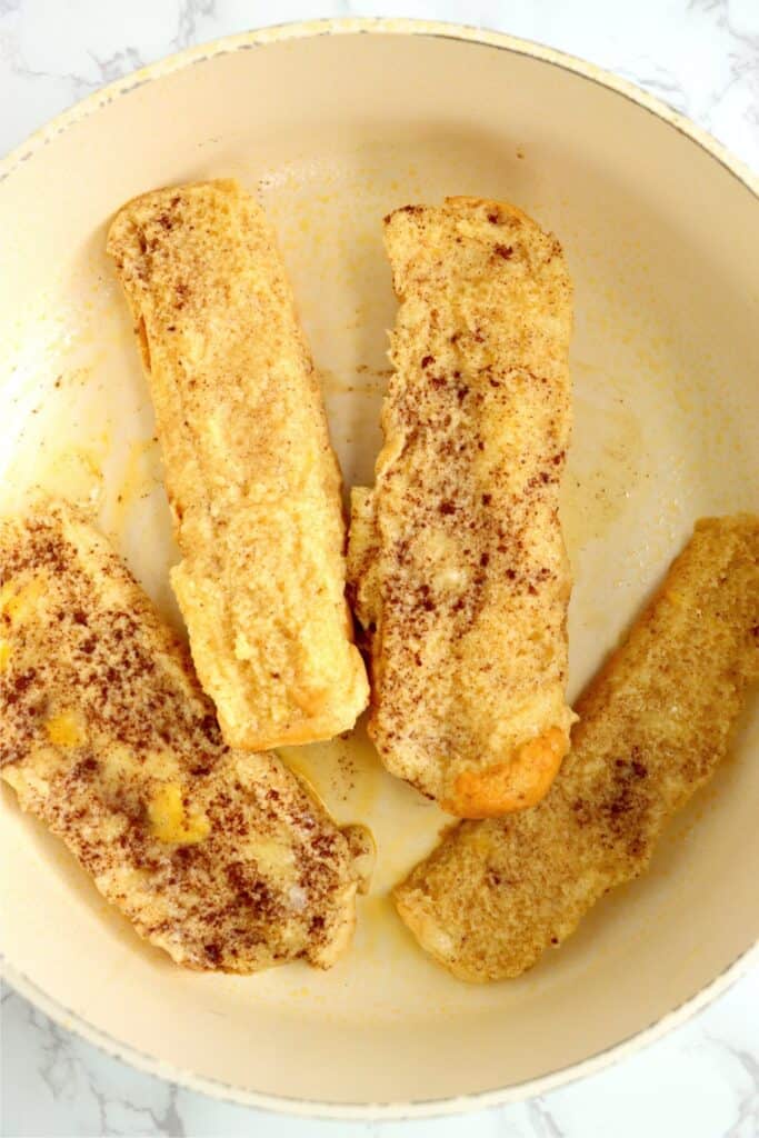 Overhead shot of uncooked hot dog bun French toast pieces in skillet