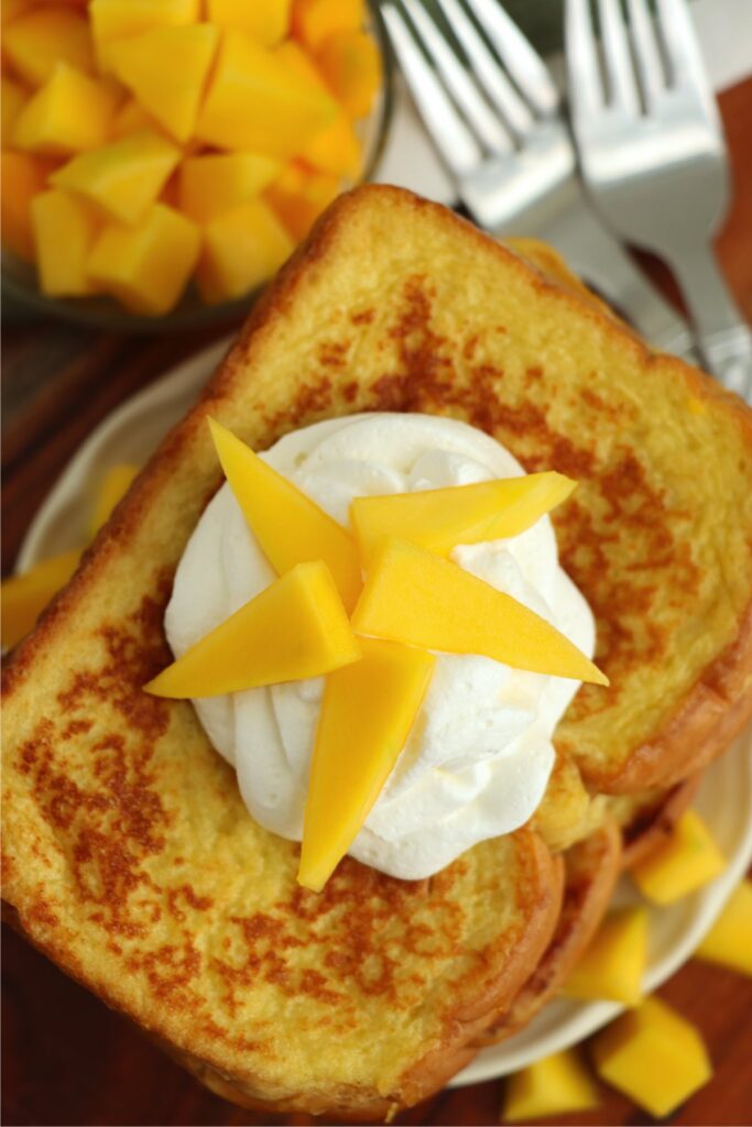 Overhead shot of mango French toast topped with whipped cream and mango slices. 