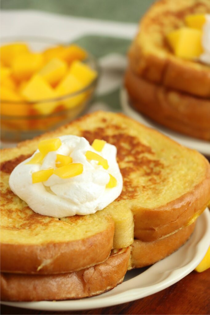 Closeup shot of mango French toast topped with whipped cream and diced mango on plate