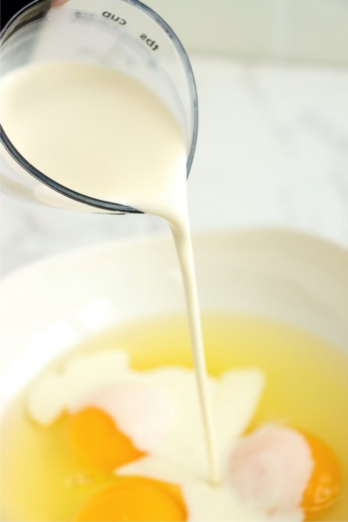 Milk being poured into bowlful of eggs