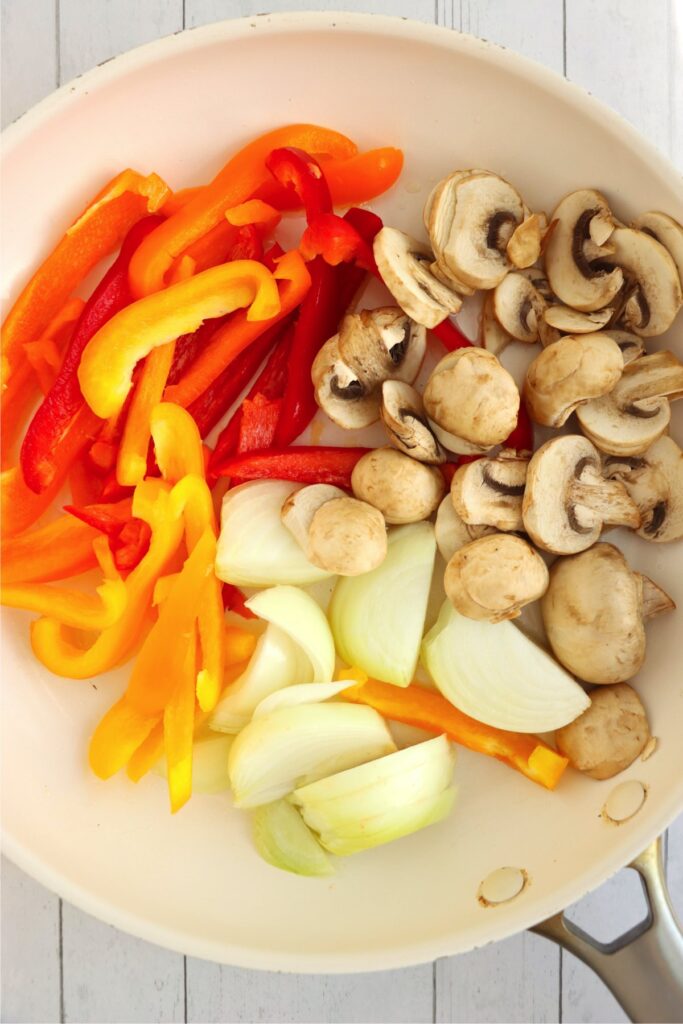 Overhead shot of sliced mushrooms, onions, and bell peppers in skillet
