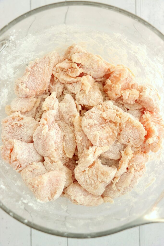 Overhead shot of flour-coated chicken chunks in mixing bowl