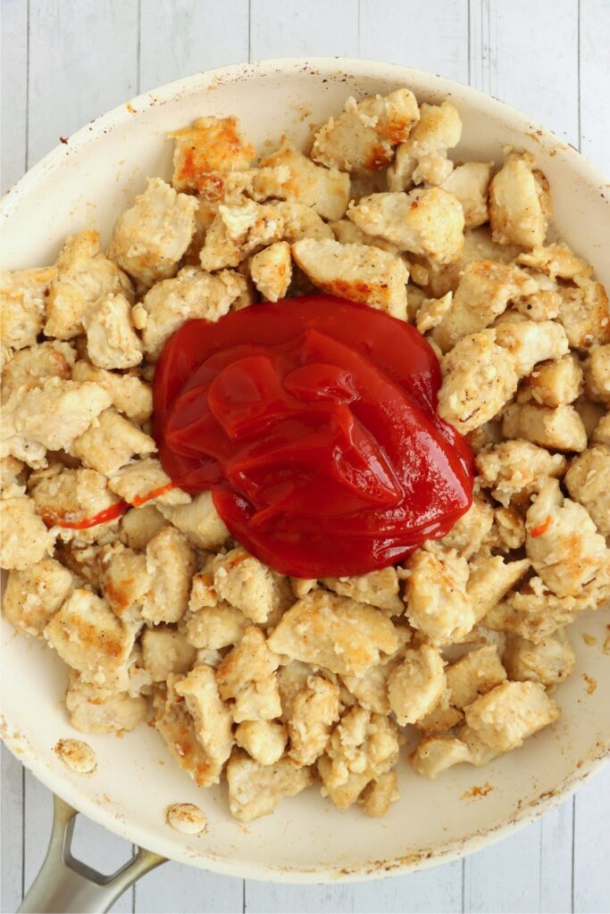 Overhead shot of ketchup topping cooked chicken in skillet
