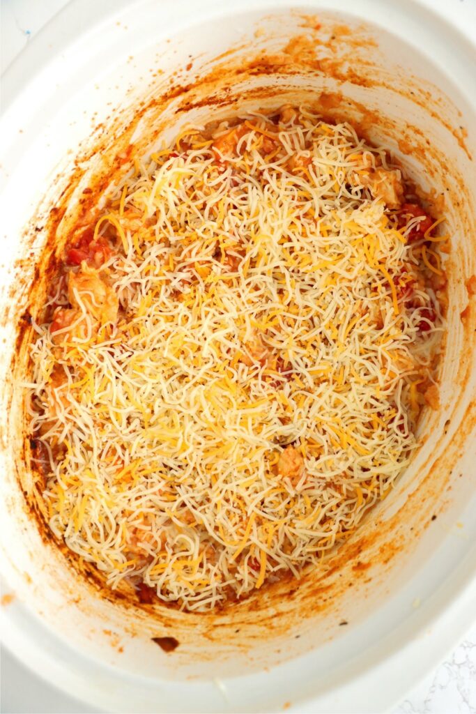 Overhead shot of taco chicken and rice in slow cooker topped with shredded cheese.