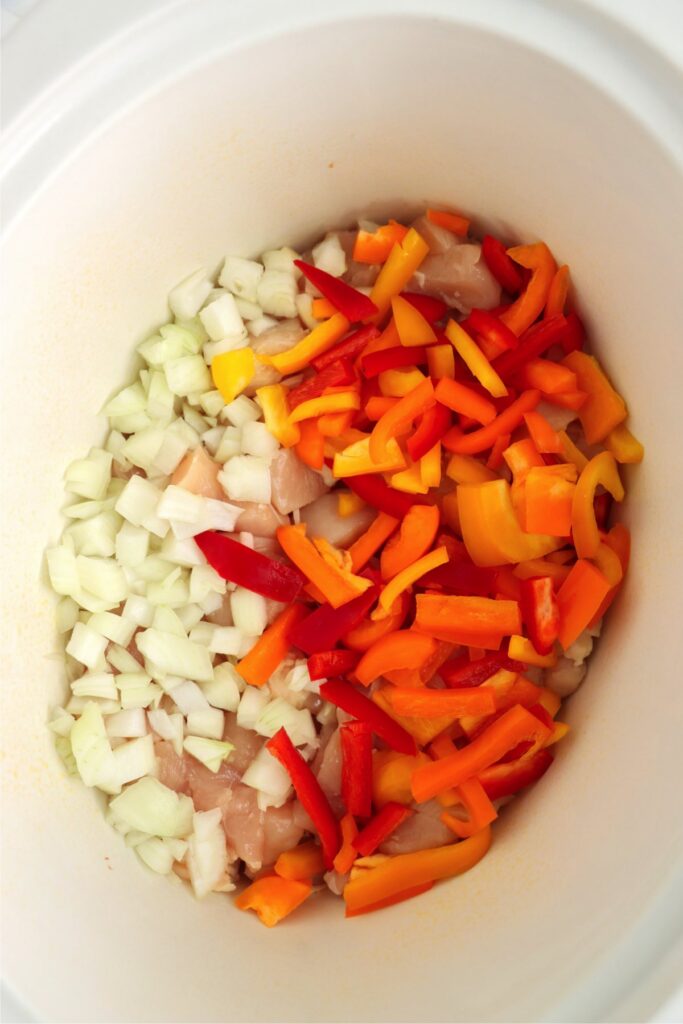 Overhead shto of chicken, bell peppers, and onions in slow cooker