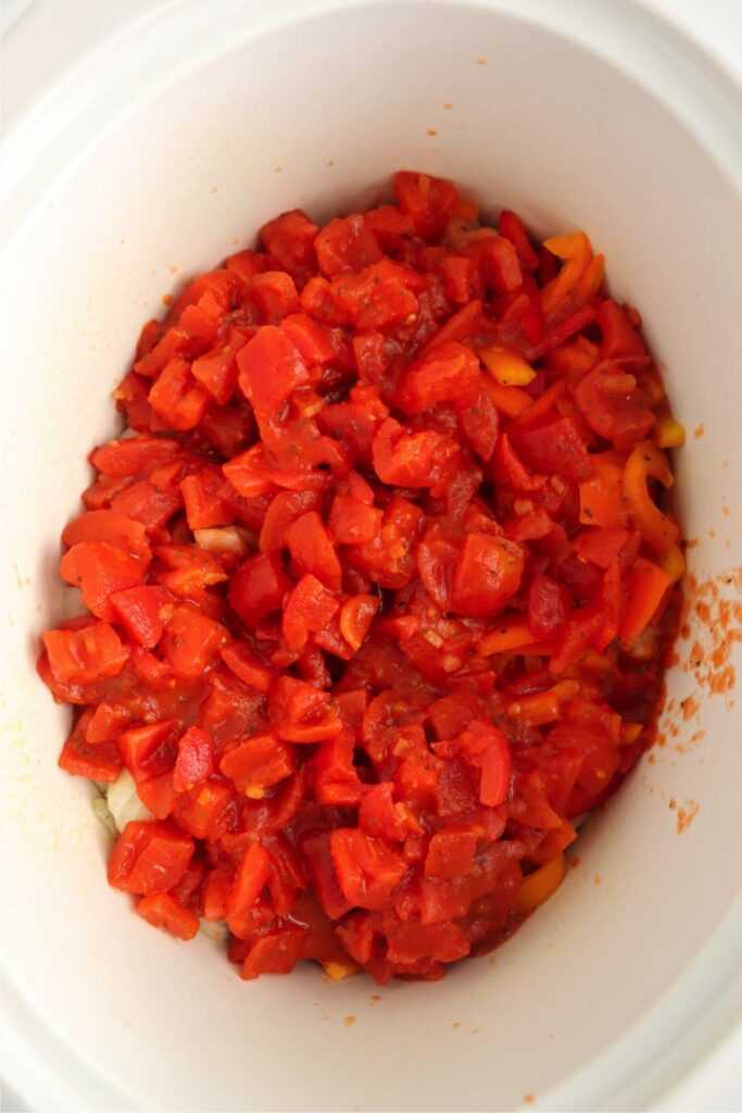 Overhead shot of diced tomatoes covering chicken and vegetables in slow cooker