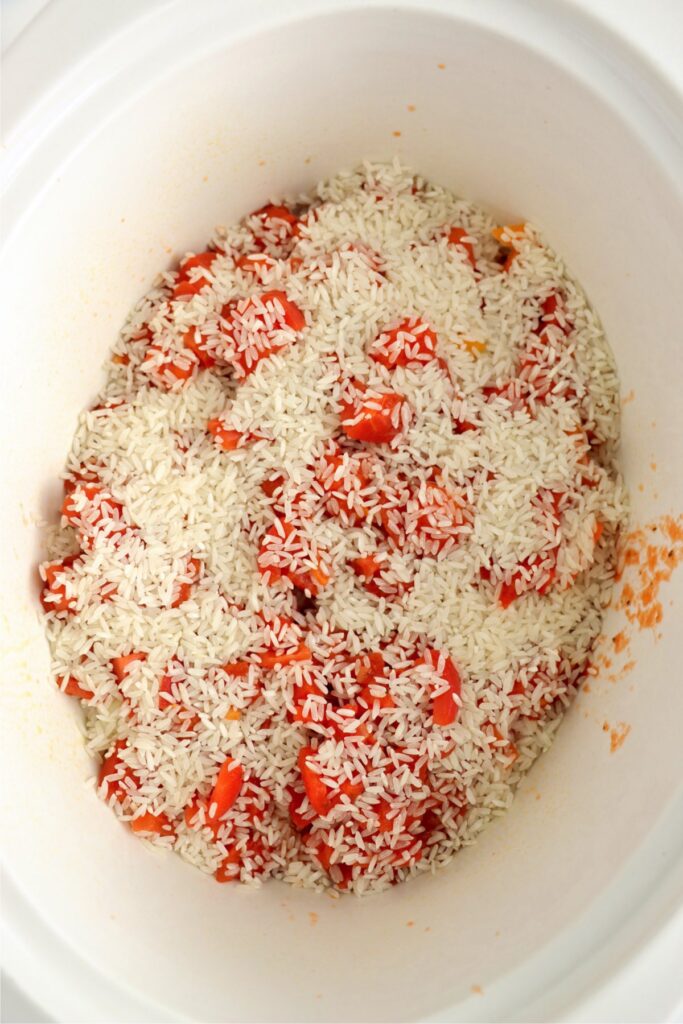 Overhead shot of rice, diced tomatoes, onions, bell peppers, and chicken in slow cooker