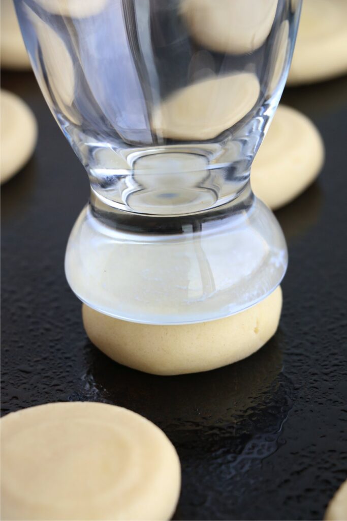 Closeup shot of cookie dough being falttened with the bottom of a glass