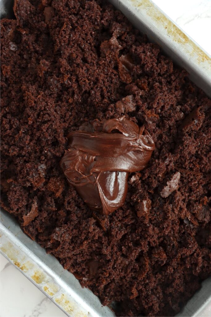 Overhead shot of frosting on top of crumbled cake in baking dish