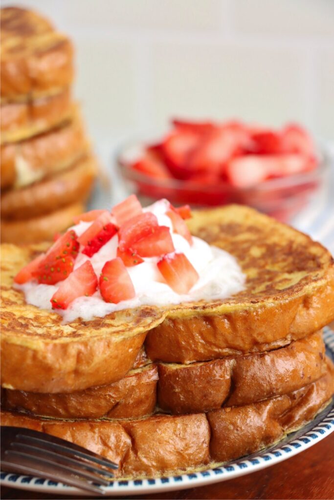 Closeup shot of stack of sweet Hawaiian bread French toast topped with whipped cream and strawberries on plate