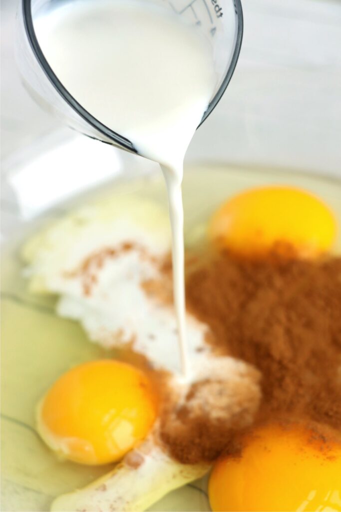 Closeup shot of creamer being poured into bowlful of eggs and cinnamon