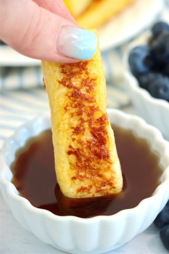 Closeup shot of hand dipping a jack in the Box French toast stick into syrup.