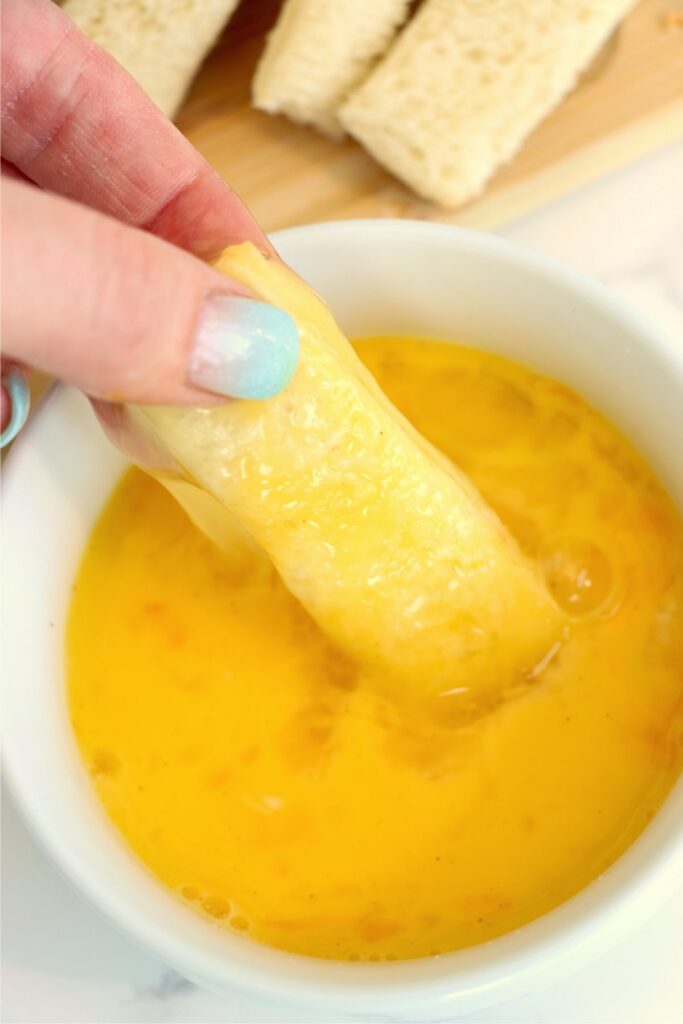 Closeup shot of hand dipping a strip of bread in egg mixture. 