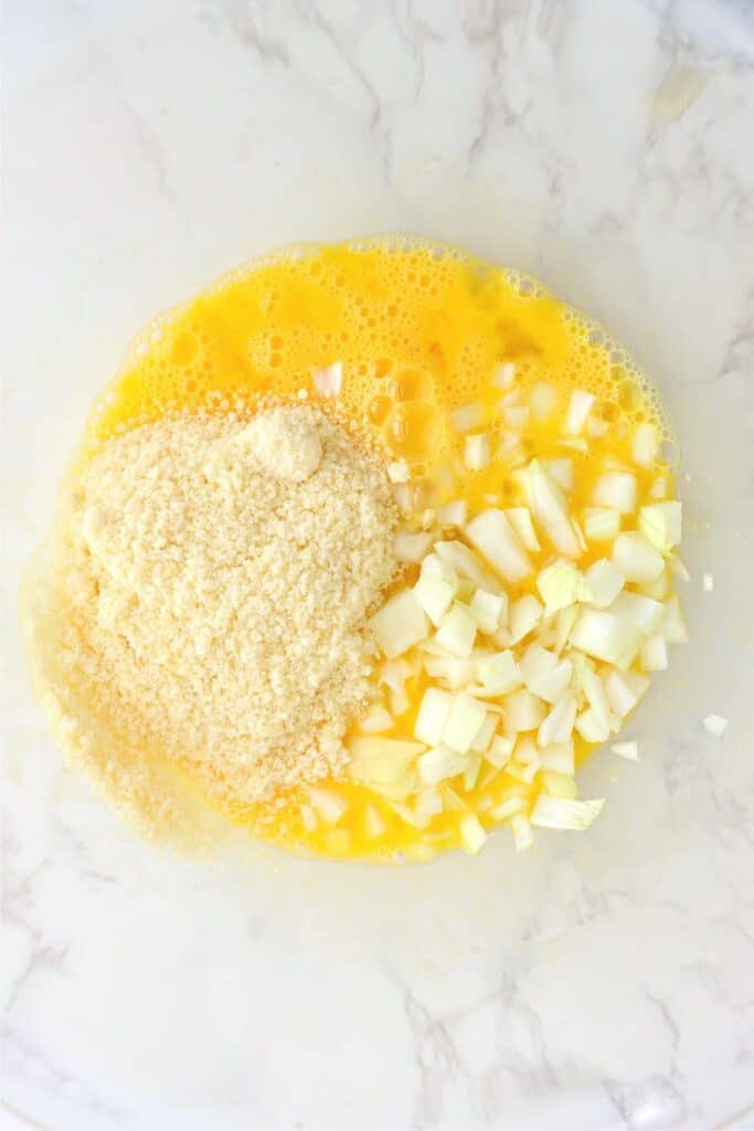 Overhead shot of eggs, onions, and parmesan cheese in mixing bowl.