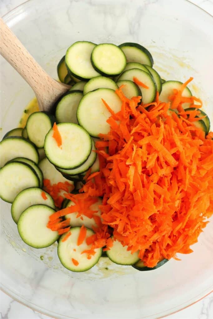 Closeup overhead shot of slice zucchini and shredded carrots in bowl with eg mixture. 