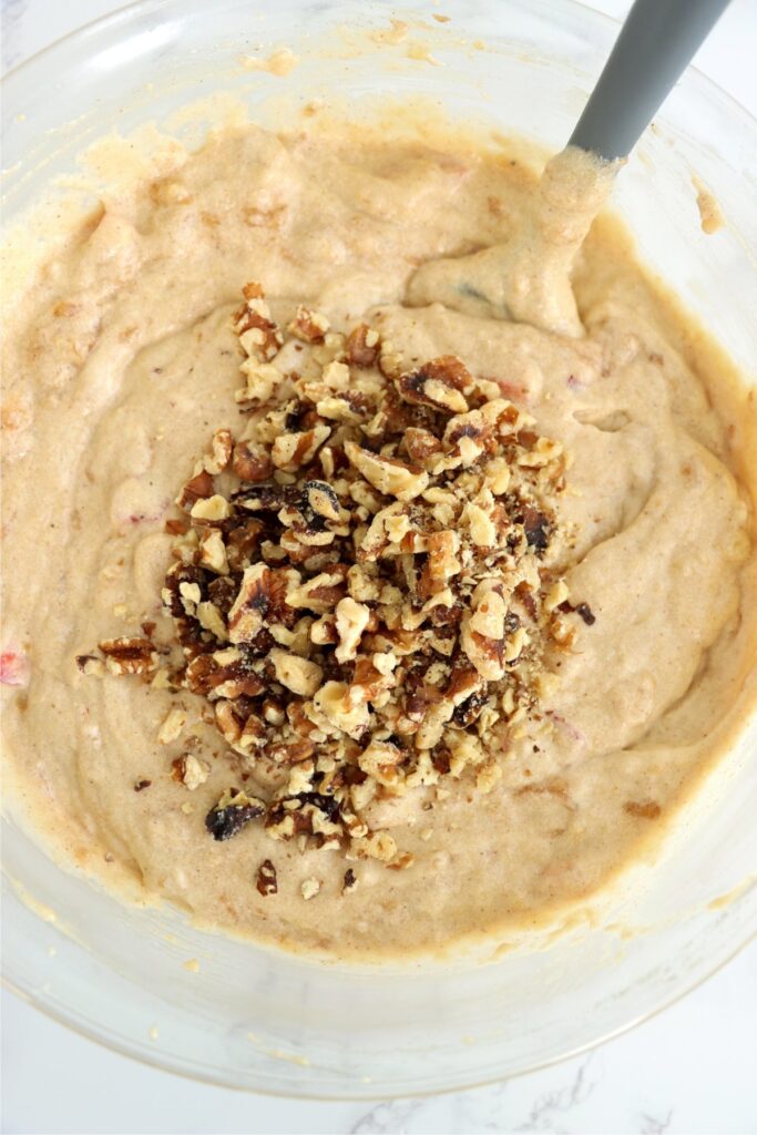 Overhead shot of chopped pecans on top of strawberry banana cake batter in bowl