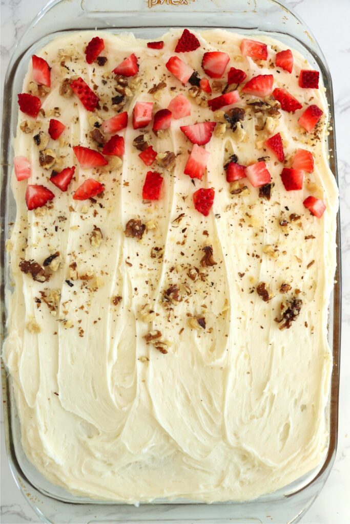 Overhead shot of frosted strawberry banana cake with half of it covered in diced strawberries and chopped pecans