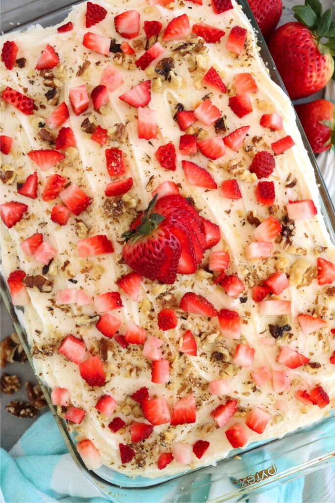 Overhead shot of frosted strawberry banana cake topped with diced strawberries and chopped pecans. 