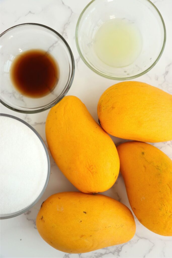 Overhead shot of individual homemade mango jam ingredients in bowls on table