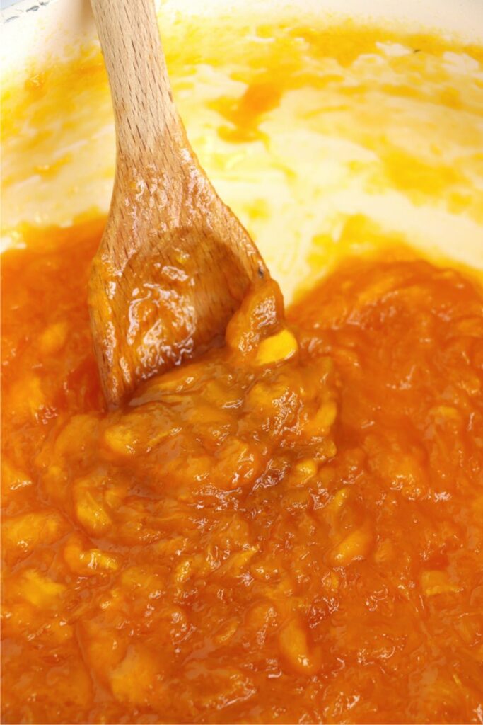 Closeup shot of spoon stirring homemade mango jam in pot