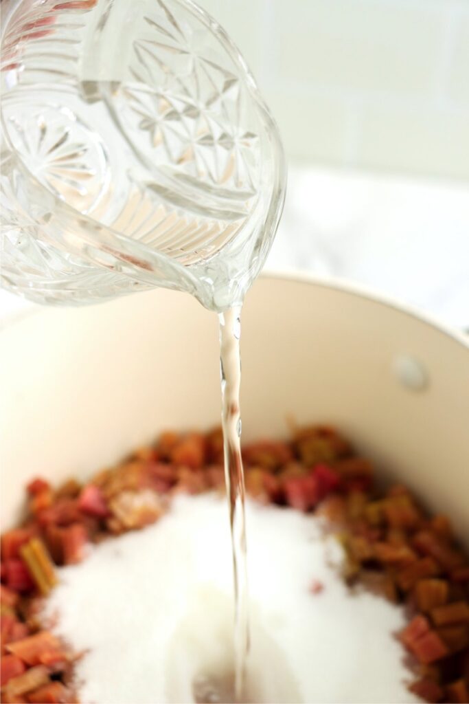 Water being poured into saucepan of sugar and rhubarb.