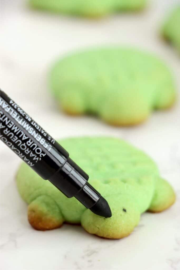 Closeup shot of black edible marker being used to draw eyes on a sea turtle sugar cookie