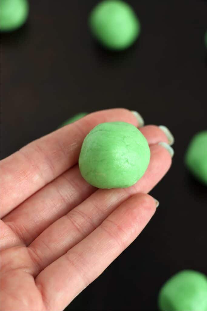 Closeup shot of hand holding a ball of green sugar cookie dough.