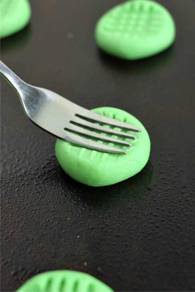 Closeup shot of fork flattening green sugar cookie dough balls on baking sheet