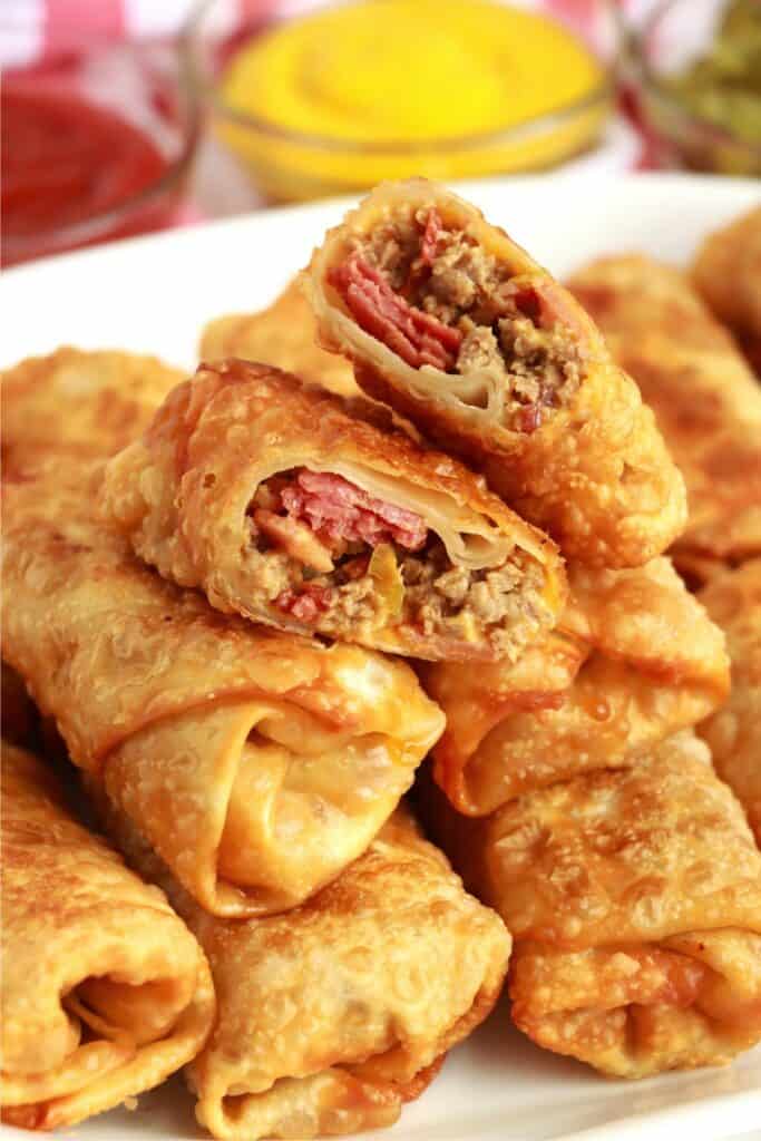 Closeup shot of bacon cheeseburger egg rolls stacked on a plate with top egg roll cut in half