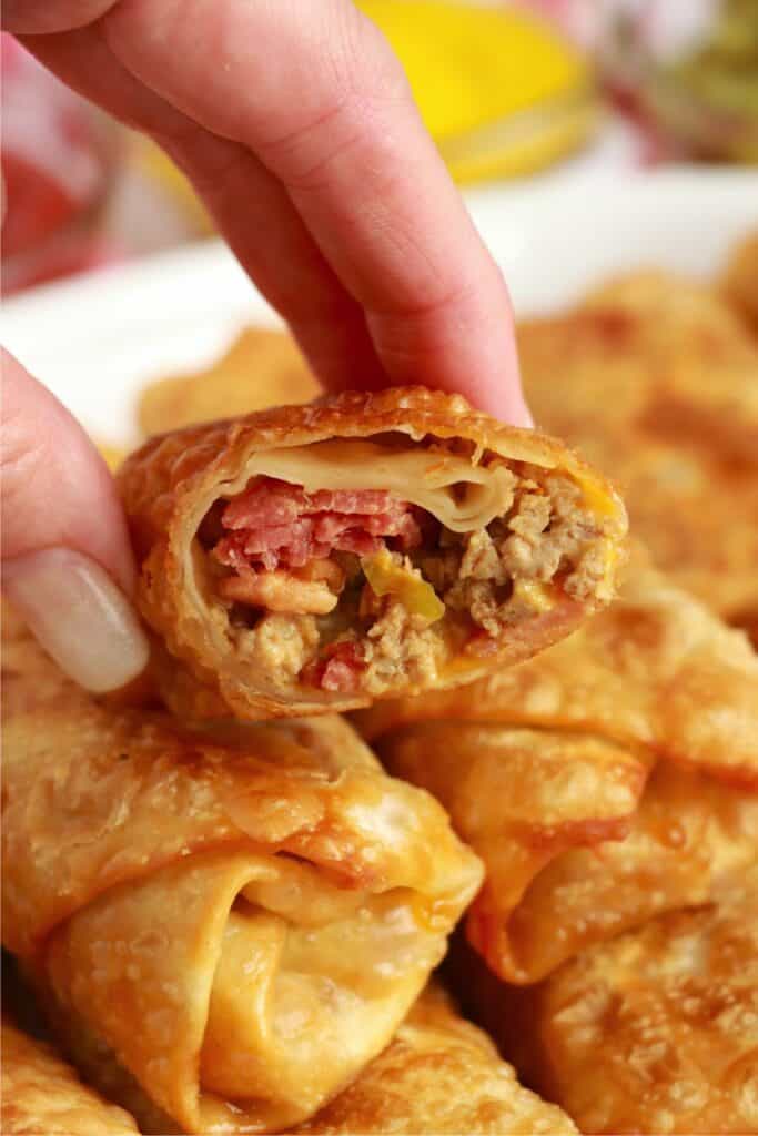 Closeup shot of hand holing bacon cheeseburger egg roll with bite taken out