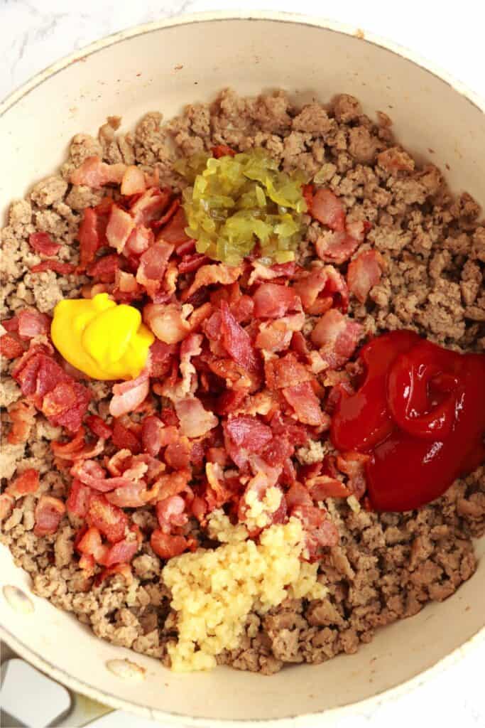 Closeup overhead shot of cooked meat, bacon, relish, kethcup, mustard, and garlic in skillet