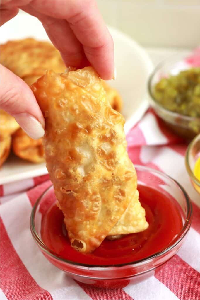 Closiong shot of bacon cheeseburger egg roll being dipped into bowl of ketchup.