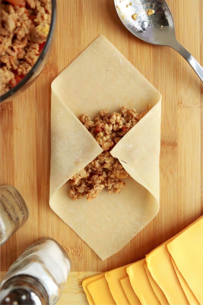 Overhead shot of two corners of egg roll wrapper foled over the bacon cheeseburger filling