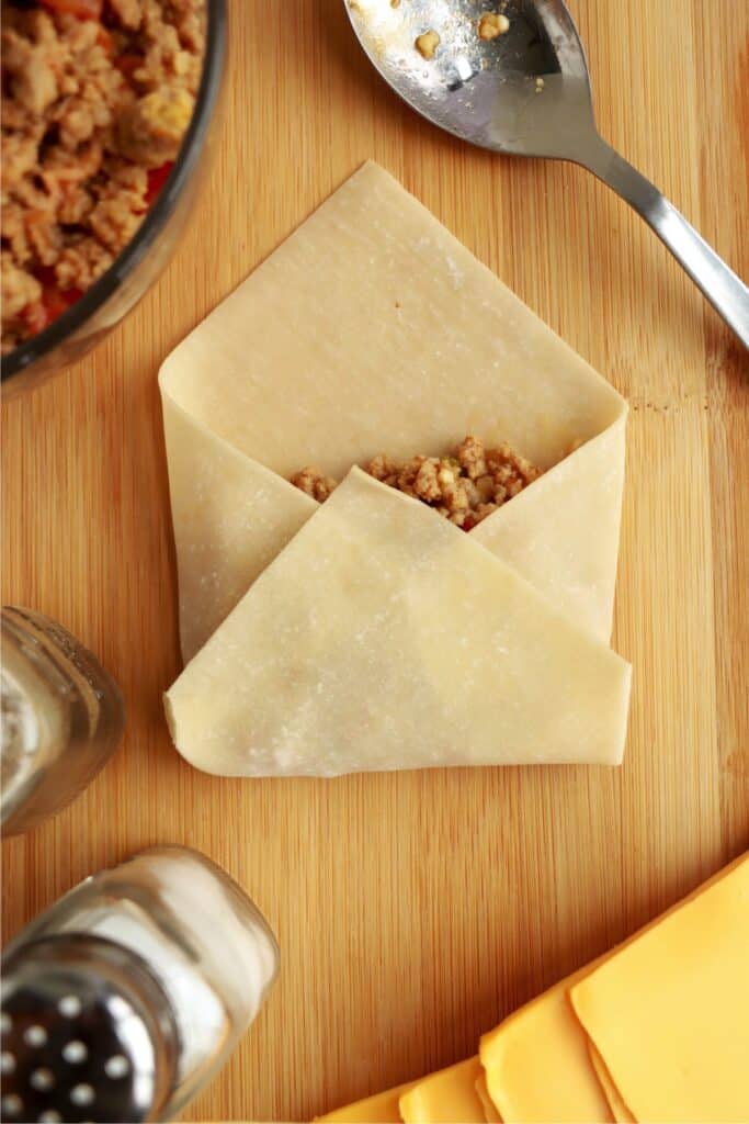 Overhead shot of both sides and bottom corner of egg roll wrapper foled over filling