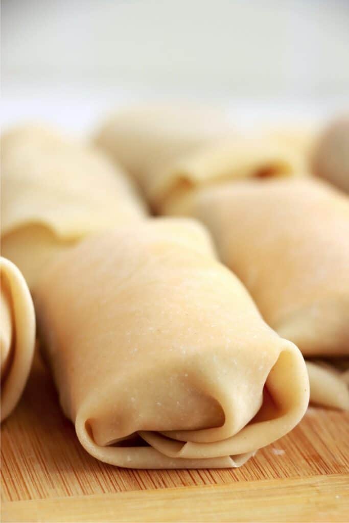 Closeup shot of uncooked bacon cheeseburger egg rolls on cutting board. 