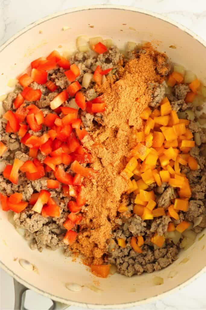 Overhead shot of cooked meat and onions with diced bell peppers and taco seasoning in skillet. 