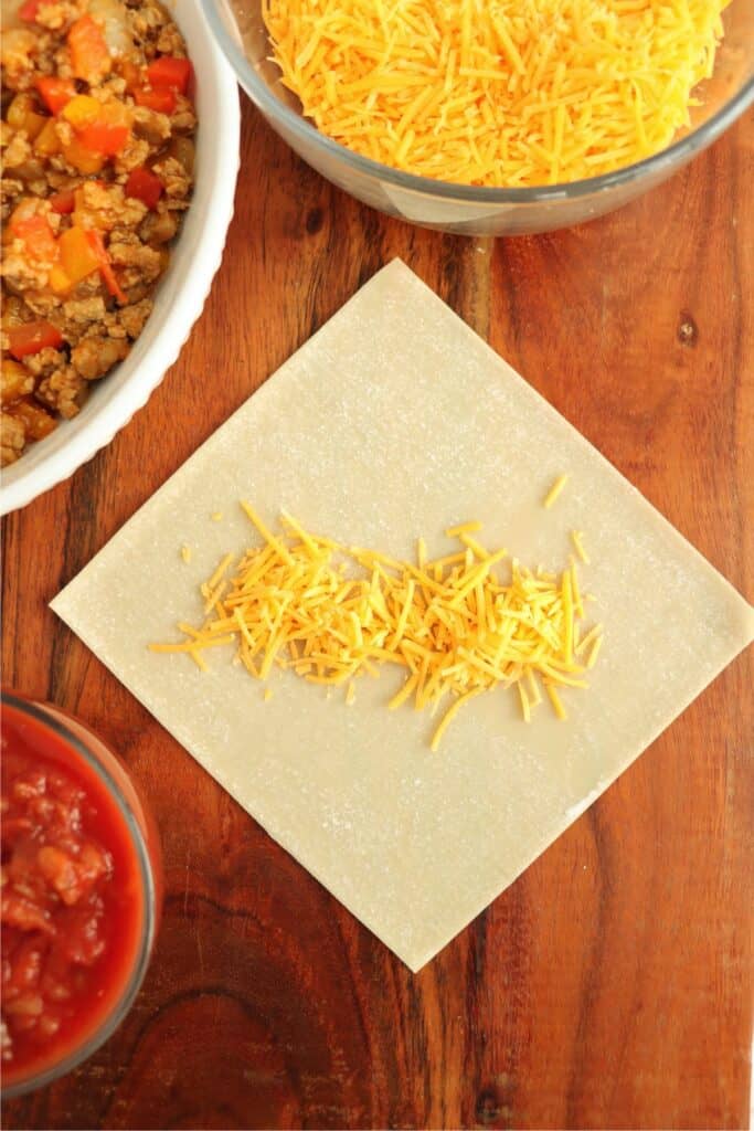 Overhead shot of shredded cheese on egg roll wrapper