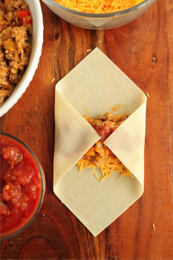 Overhead shot of two corners of egg roll wrapper folded over the filling